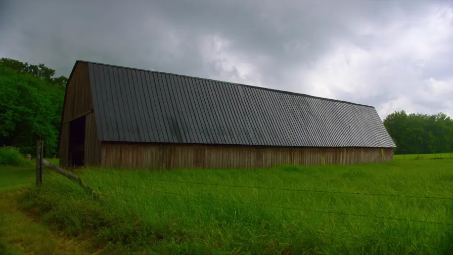 Weathered board barn with a dark standing seam metal roof in a Missouri pasture under storm cloud