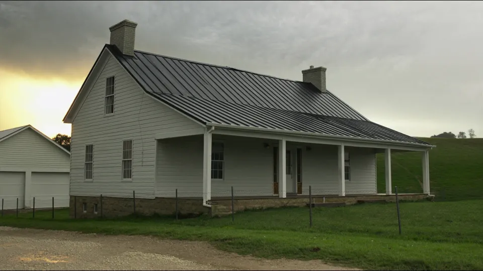 White clapboard Missouri farmhouse with a dark standing seam metal roof under storm cloud